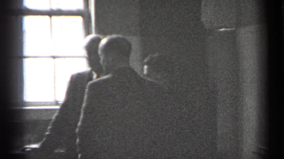 Suited men cluster near a bright window, with faces partly obscured by backlight in 1944 San Francisco footage.