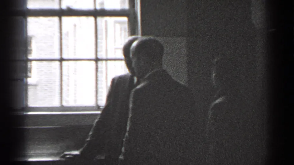 A small group of suited men stands near a multi-pane window inside a dim San Francisco room in 1944 footage.