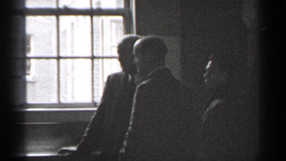 1944 San Francisco home-movie frame showing adults in dark silhouette near a large interior window.