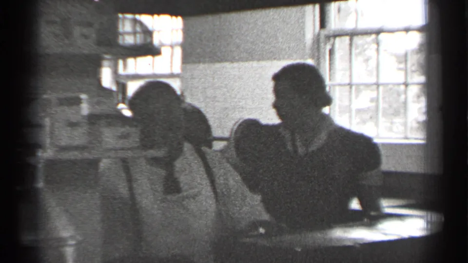 Adults in period dress sit or stand at a table inside a backlit San Francisco interior.
