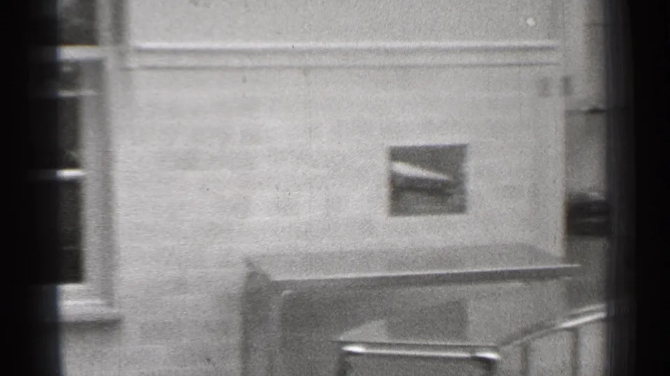 1944 San Francisco 8mm frame showing a plain institutional wall, small framed picture, and metal table or cabinet.