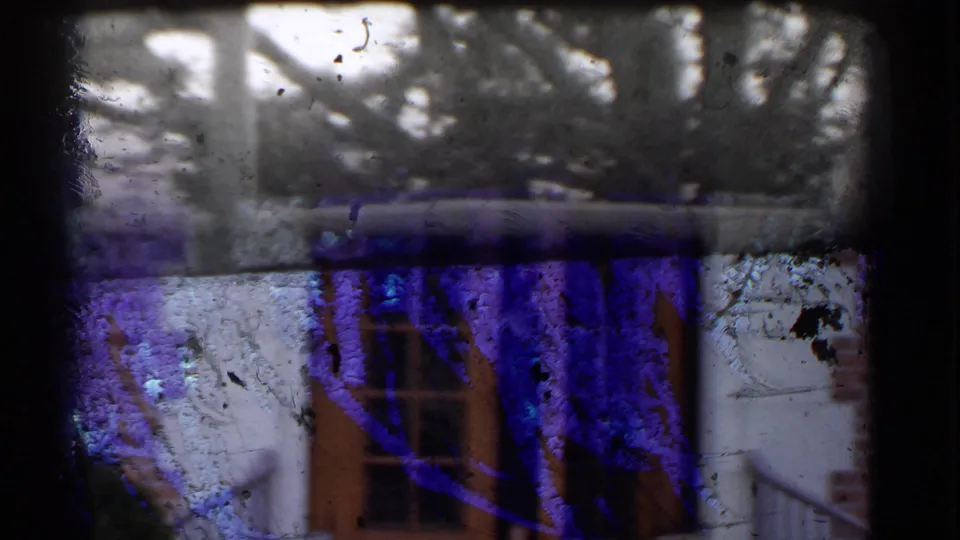 Obscured 8mm exterior frame with branches and railing, showing heavy color shift and physical film wear.