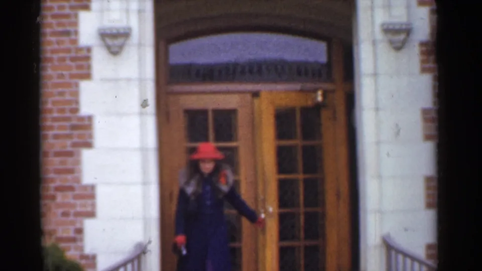 In supported 1944 San Francisco footage, a woman in a red hat and dark coat stands at a brick and stone residential doorway.