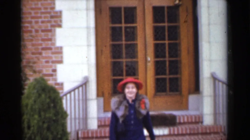 The woman smiles toward the camera while descending steps from a brick and stone San Francisco house in supported 1944 footage.