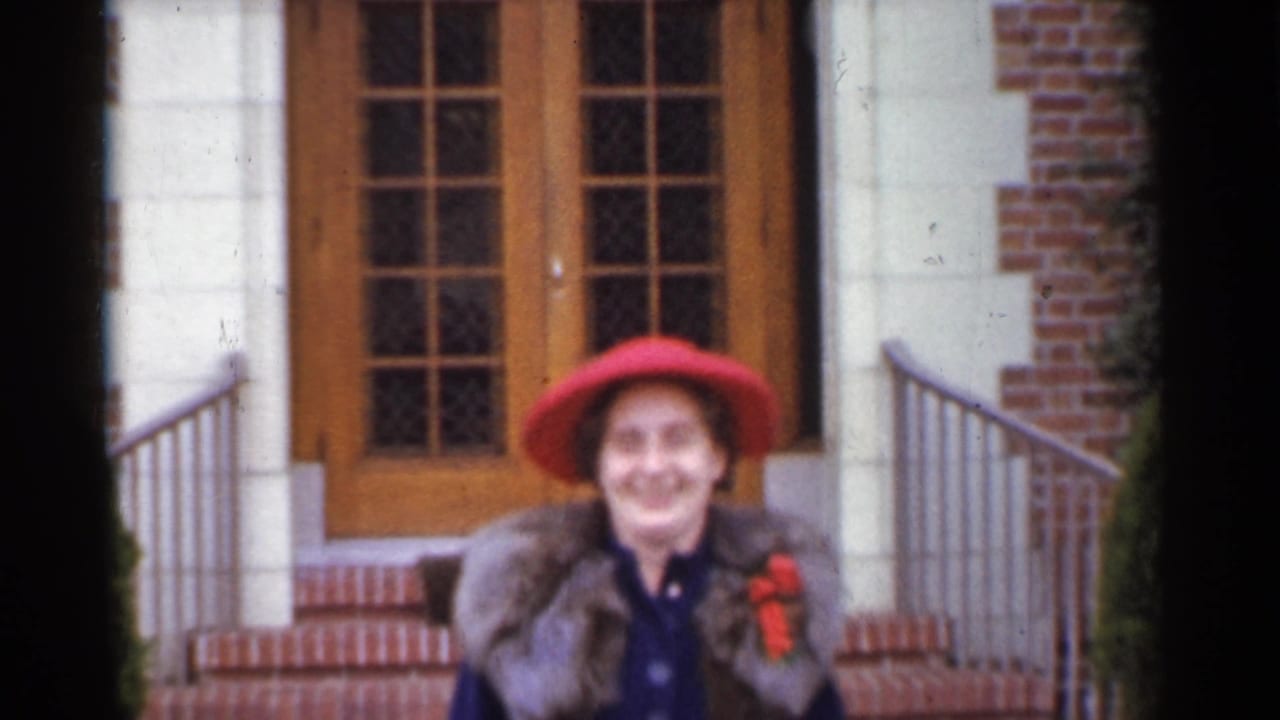 Smiling older woman in a red hat stands near steps outside a brick building entrance.