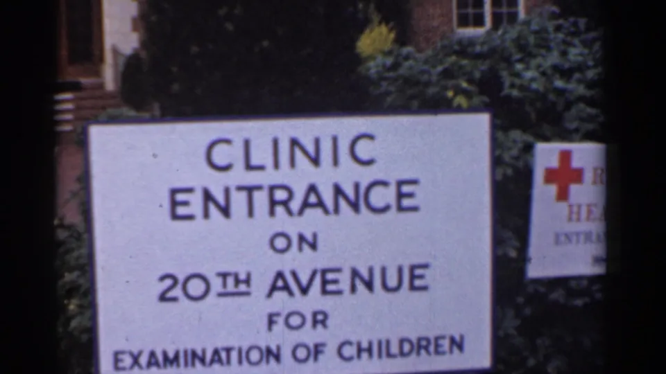 The camera frames the 20th Avenue clinic entrance sign for children's examinations, with greenery and a Red Cross-style emblem at right.