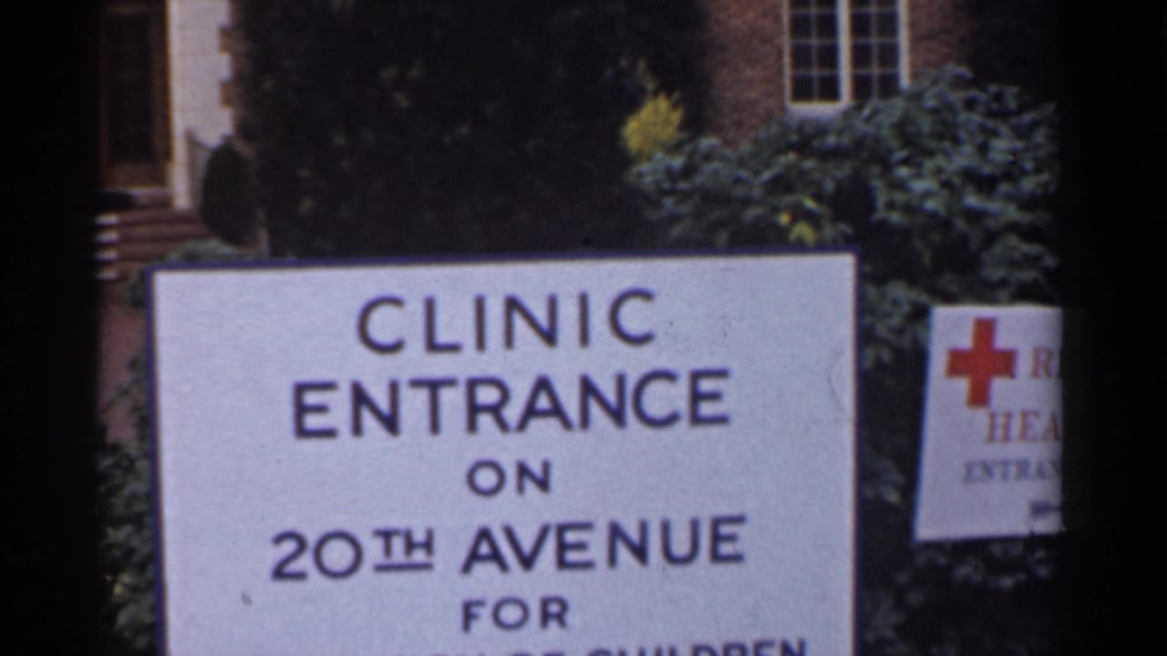 1944 San Francisco frame showing a white clinic entrance sign on 20th Avenue with trees, shrubs, and a brick building behind it.