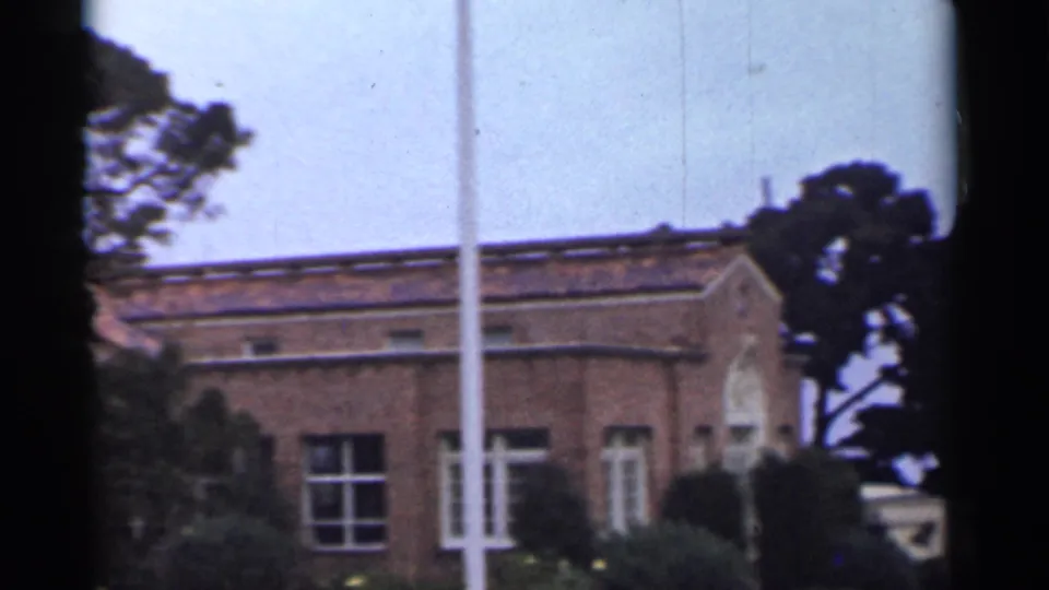 1944 San Francisco frame with a partial red cross clinic sign, brick institutional building, trees, windows, and a white pole.