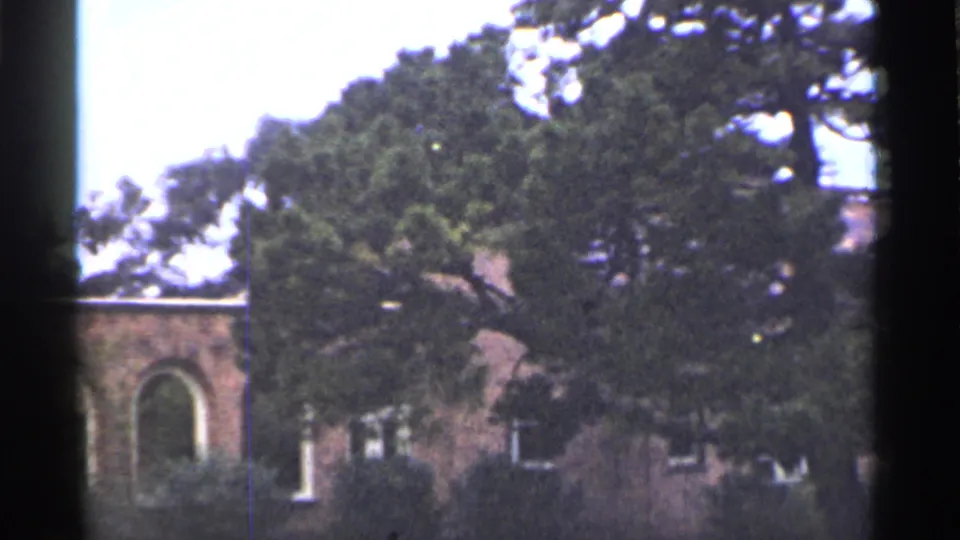 1944 San Francisco frame looking across trees and shrubs toward a brick building with an arched doorway on clinic grounds.