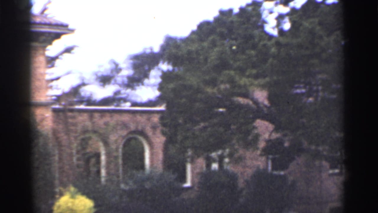 1944 San Francisco 8mm frame showing a brick building with arched openings, trees, shrubs, and heavy dark borders from the film scan.