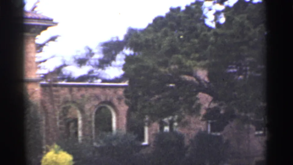 1944 San Francisco 8mm frame showing a brick building with arched openings, trees, shrubs, and heavy dark borders from the film scan.