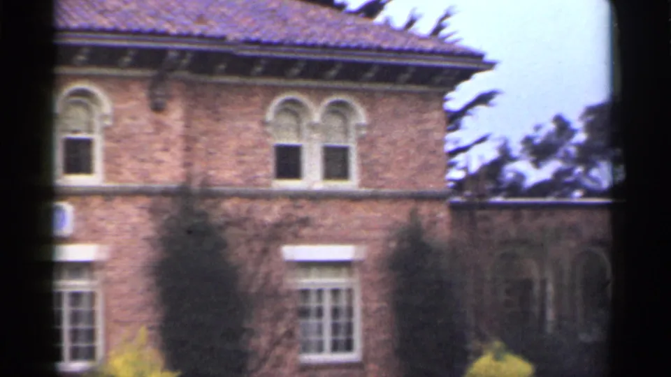 1944 San Francisco exterior frame of a brick building corner with clay roof tiles, arched upper windows, ivy, and trees behind it.