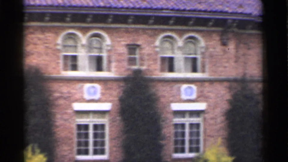 1944 San Francisco 8mm frame showing a closer brick facade with paired arched windows, divided-light lower windows, ivy, and plantings.