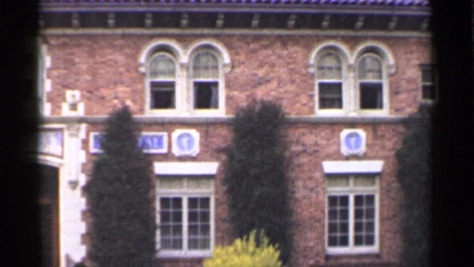 1944 San Francisco frame of the brick exterior with several arched windows, dark ivy growth, shrubs, and divided-light lower windows.