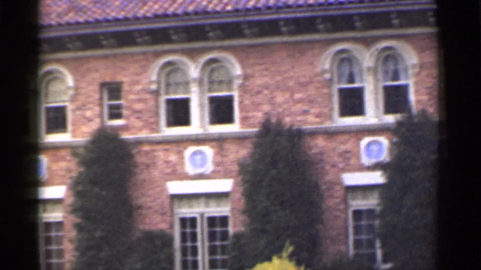 1944 San Francisco home-movie view of the red brick wall, paired arched windows, blue facade emblems, awnings, and trees.
