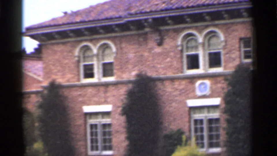 1944 San Francisco frame with the upper brick facade, arched windows, a blue circular emblem, trees, and a clay-tile roof edge.