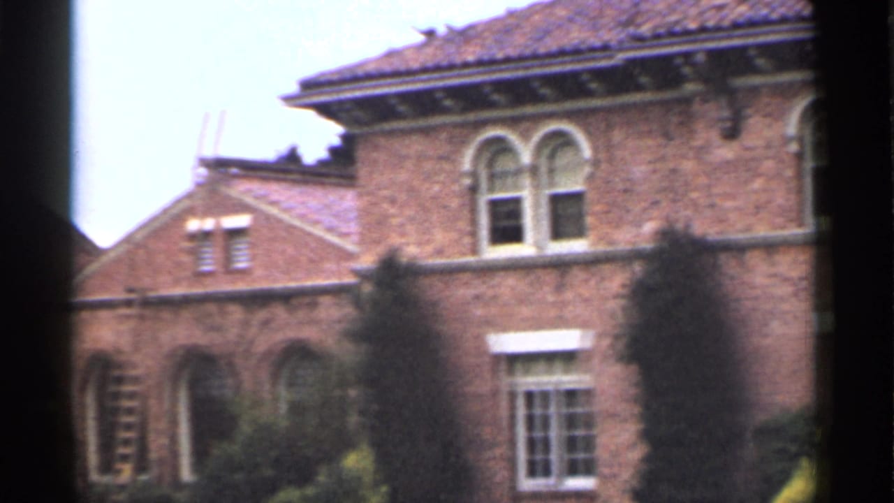 Brown brick building with arched windows, tiled roof, shrubs, and dark film-edge obstruction.
