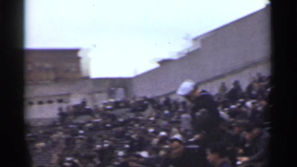 1944 San Francisco frame showing crowded outdoor bleachers, bundled spectators, and masonry structures during a public event.