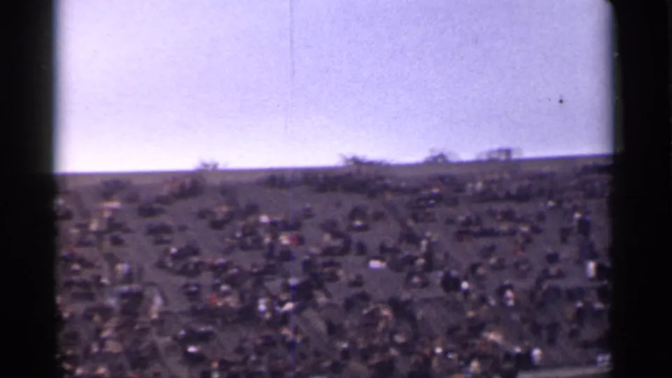 1944 San Francisco home-movie frame showing a distant crowd spread across a sloped hillside lawn under a pale sky.