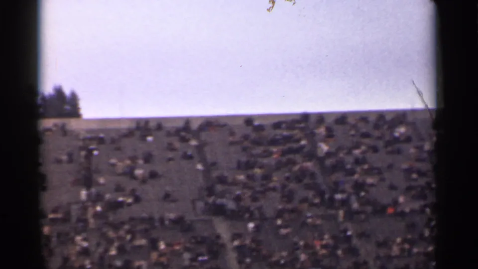 1944 home-movie frame showing a distant public crowd on a San Francisco hillside, with trees near the left horizon.