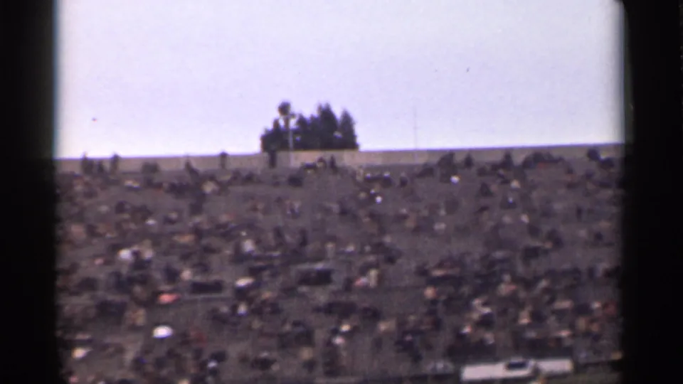 Wide 8mm frame of a San Francisco hillside crowd, with a small group of trees silhouetted near the ridge.