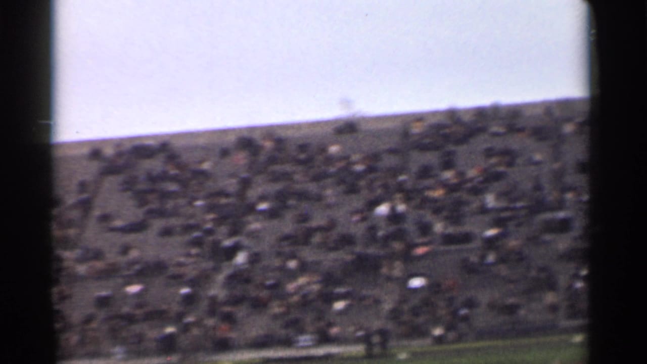 1944 San Francisco 8mm frame showing distant spectators packed across stadium bleachers above a narrow green field edge.