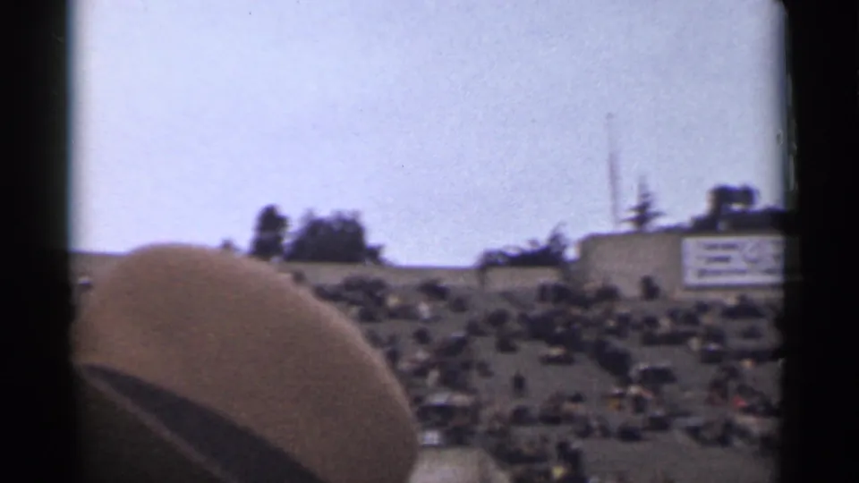 1944 San Francisco home-movie frame showing a broad hillside audience with distant buildings or signage and dark film borders.