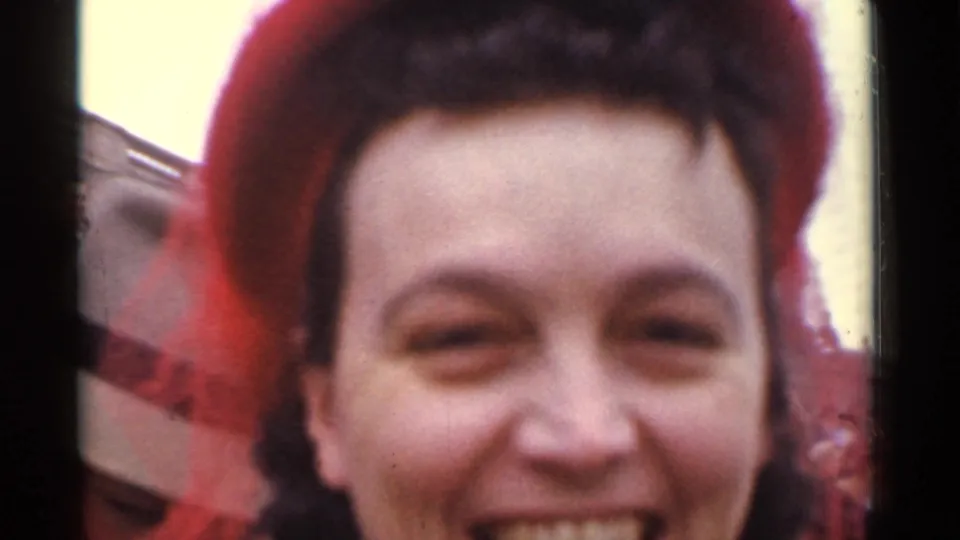 1944 San Francisco frame showing a smiling woman in red headwear, with another spectator's hat partly visible at the edge.