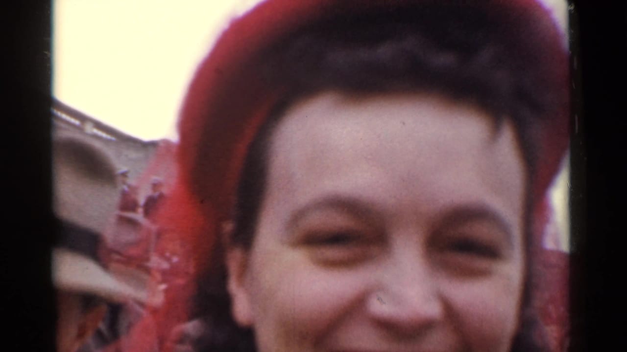 Smiling woman in a red hat close to the camera at an outdoor crowd event.