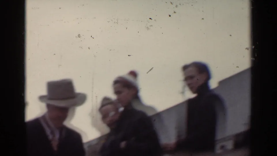 A small group of adults, including a man in a fedora and people in coats, stands before a crowd in the 1944 San Francisco footage.
