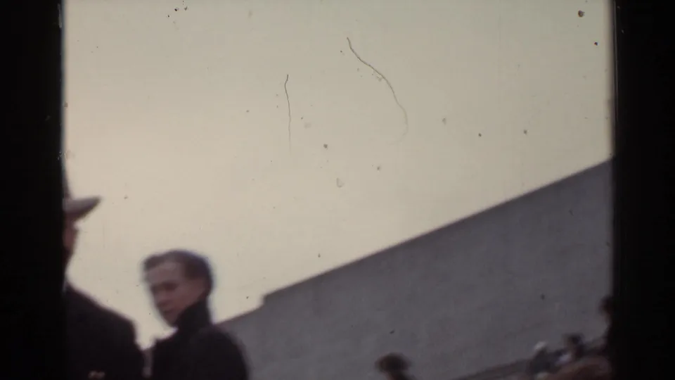 1944 San Francisco home-movie frame showing people near a stadium area, including a partially framed man and a woman in dark clothing.
