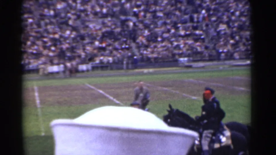 Spectator-view frame from a 1944 San Francisco football stadium, with a mounted rider near the field and packed stands beyond.