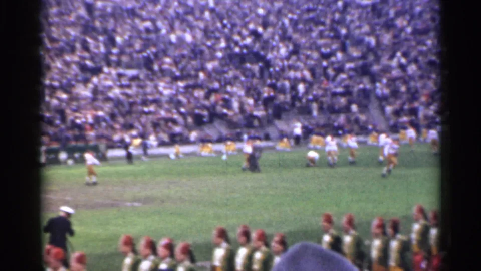 San Francisco 1944 8mm frame showing marching band members in green uniforms near the sideline as football play continues on the field.