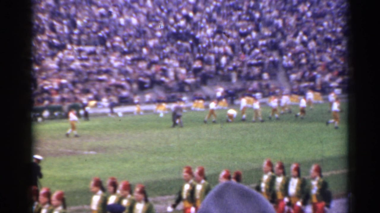 1944 San Francisco 8mm frame showing a high school football game from the stands, with band members in the foreground and a dense crowd beyond the field.