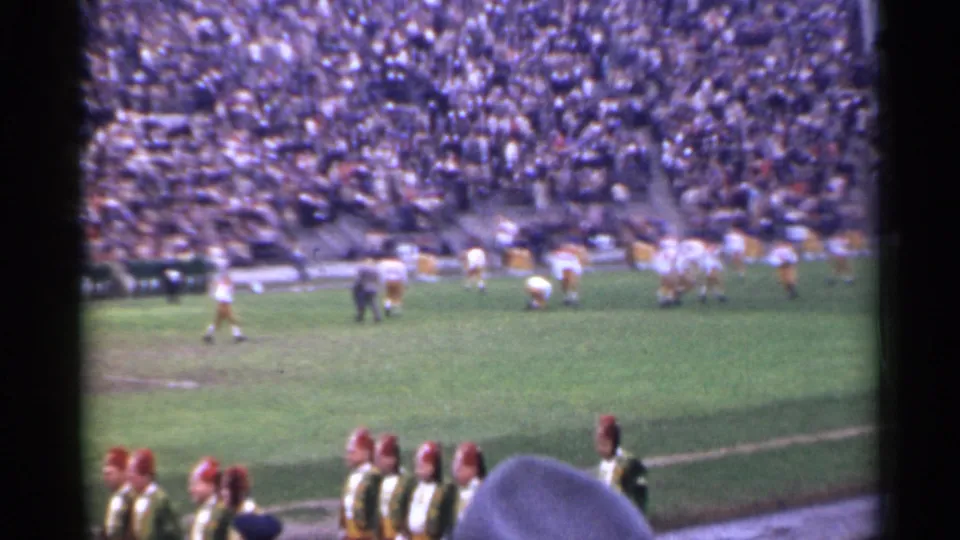 1944 San Francisco high school football scene with players spread across the field, a crowded grandstand, and marching band figures near the camera.