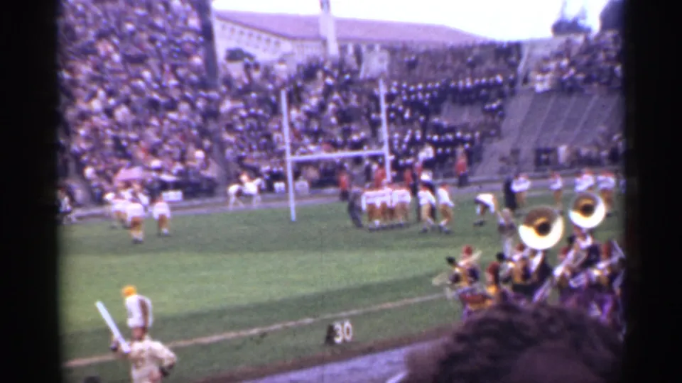 1944 San Francisco stadium frame with brass band musicians near the sideline as football players and spectators remain visible.