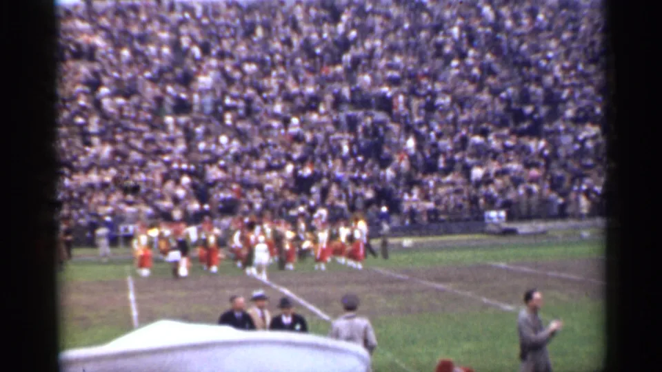 Home-movie view of a marching band on a San Francisco stadium field with packed stands behind it.