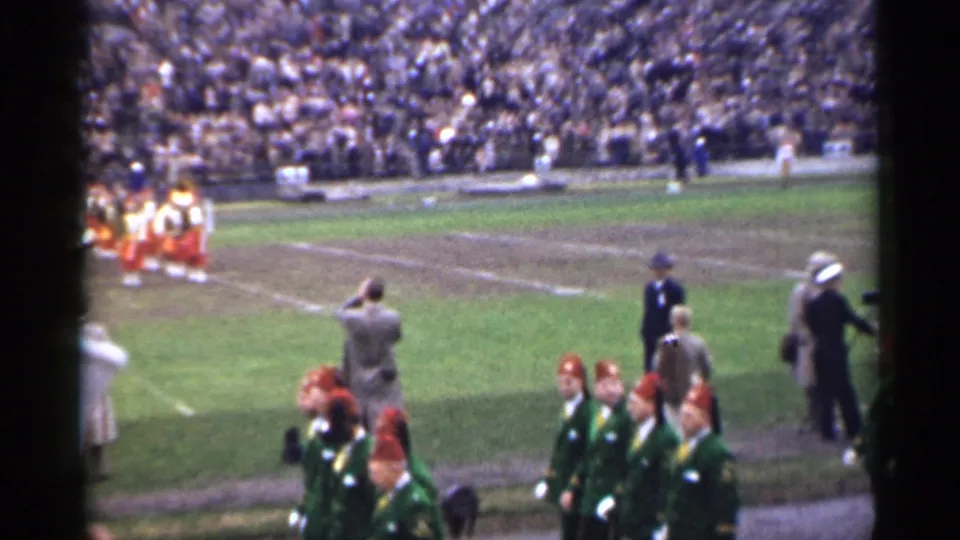 Sideline view in a 1944 San Francisco stadium with spectators, attendants, and the marching band partly visible.