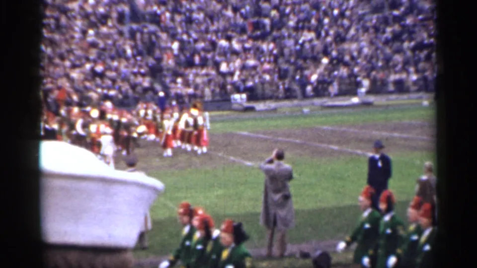 Spectator-shot 8mm frame from a 1944 San Francisco stadium, showing a marching band and crowded stands.