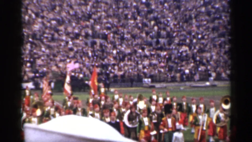 1944 San Francisco field-event frame showing a marching band with flags and brass instruments before a large stadium audience.