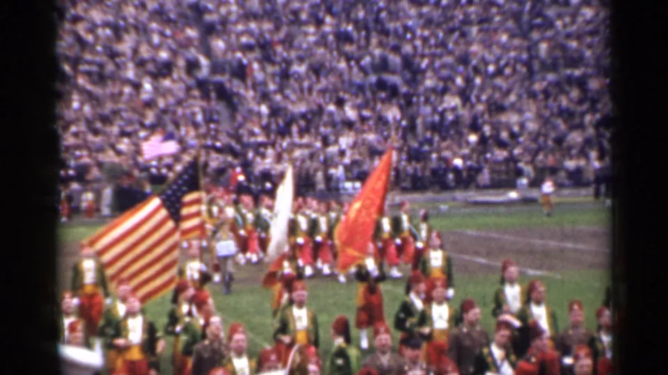 1944 San Francisco home-movie frame showing uniformed marchers, color guard flags, and packed stadium bleachers.