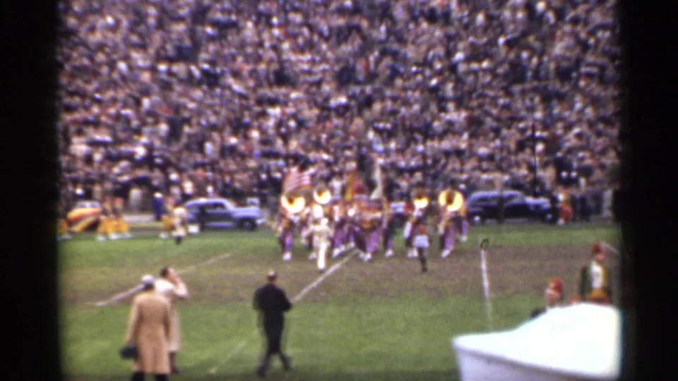 Wide 1944 San Francisco stadium view with marching band members on the field, spectators, and parked cars along the sideline.