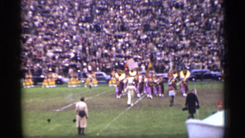 San Francisco 1944 frame showing the halftime band moving across the football field with flag and brass sections visible.
