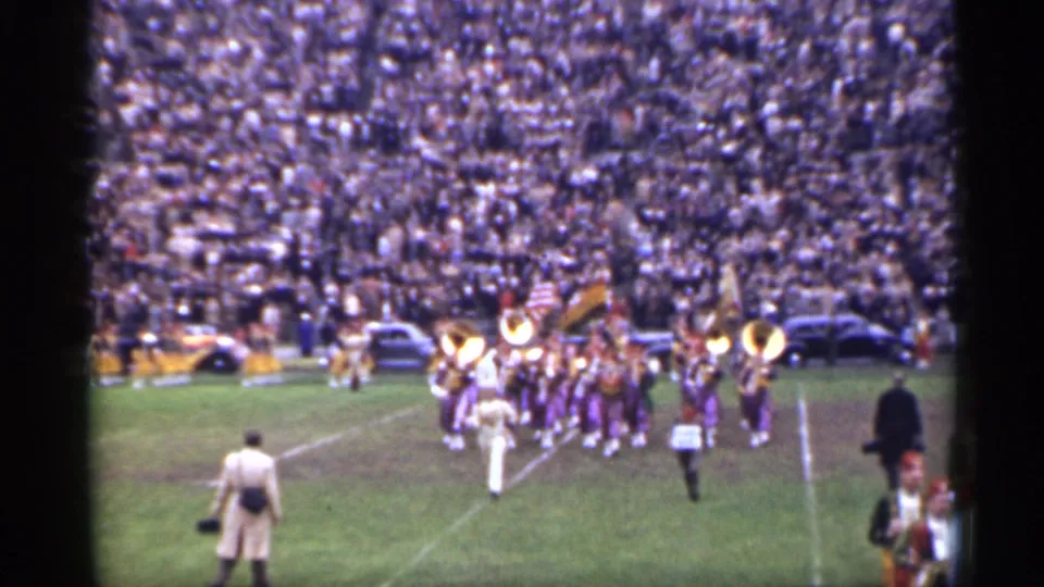 San Francisco 1944 home-movie frame of the marching band crossing the football field near sideline attendants and spectators.