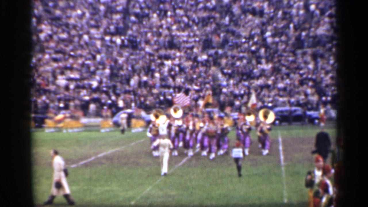 Marching band on a football field before a packed stadium crowd.