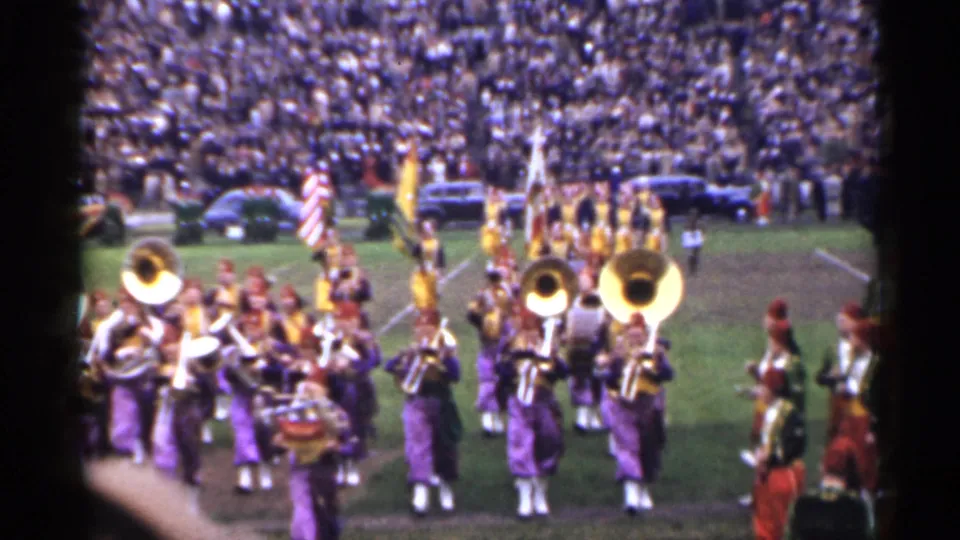1944 San Francisco stadium footage showing purple-and-gold uniformed musicians with brass and drums near flag bearers.