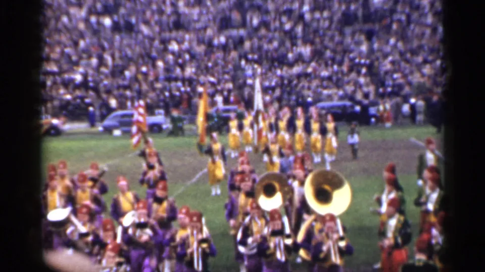 1944 San Francisco stadium frame showing band musicians in the foreground and flag-bearing marchers arranged across the field.
