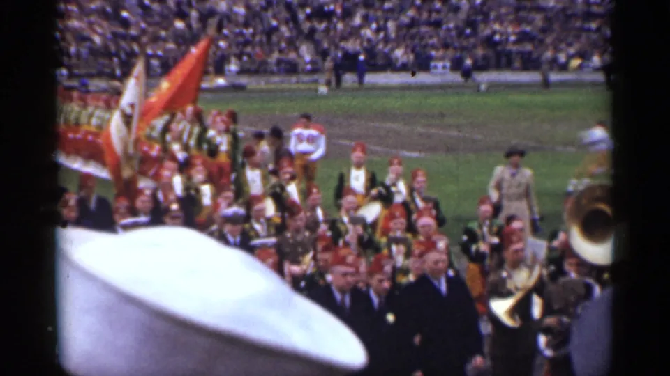 San Francisco stadium procession with flags, uniformed musicians, brass instruments, and a football player visible on the grass field.