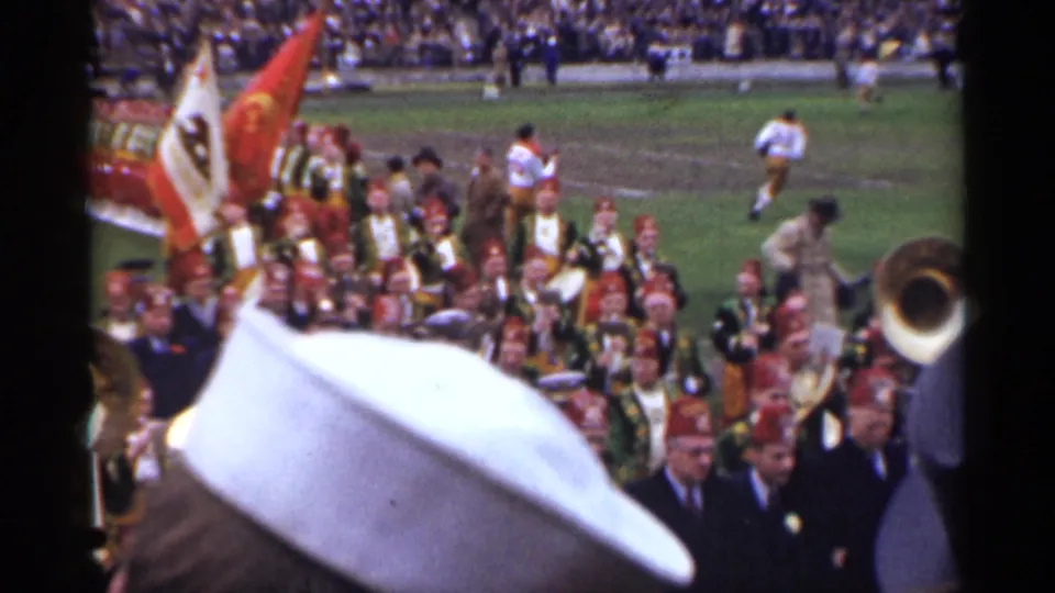1940s San Francisco stadium ceremony showing a dense marching band group, flags, spectators, and football players in the background.
