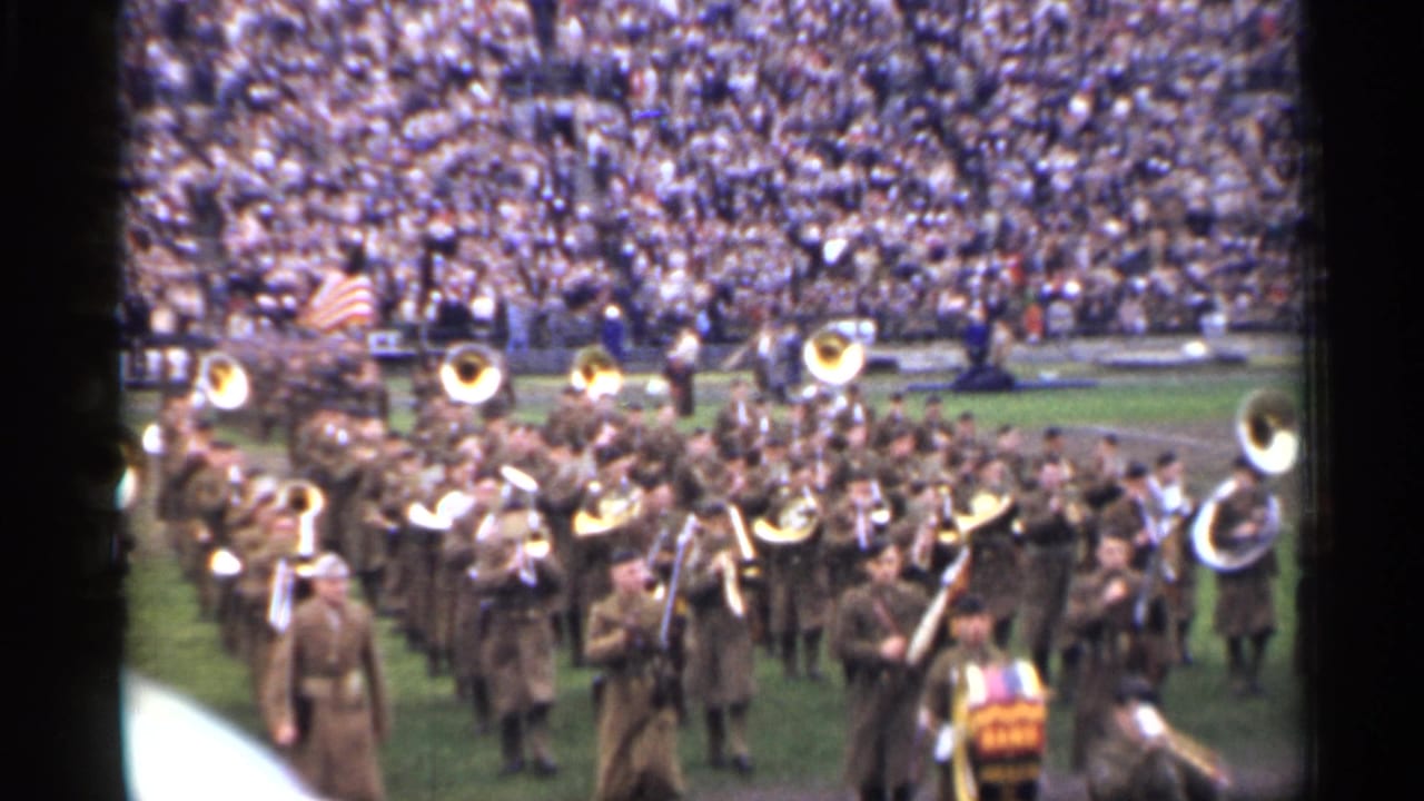 Uniformed military band performs on a San Francisco stadium field in the stated 1944 home-movie footage, with brass instruments and spectators visible.